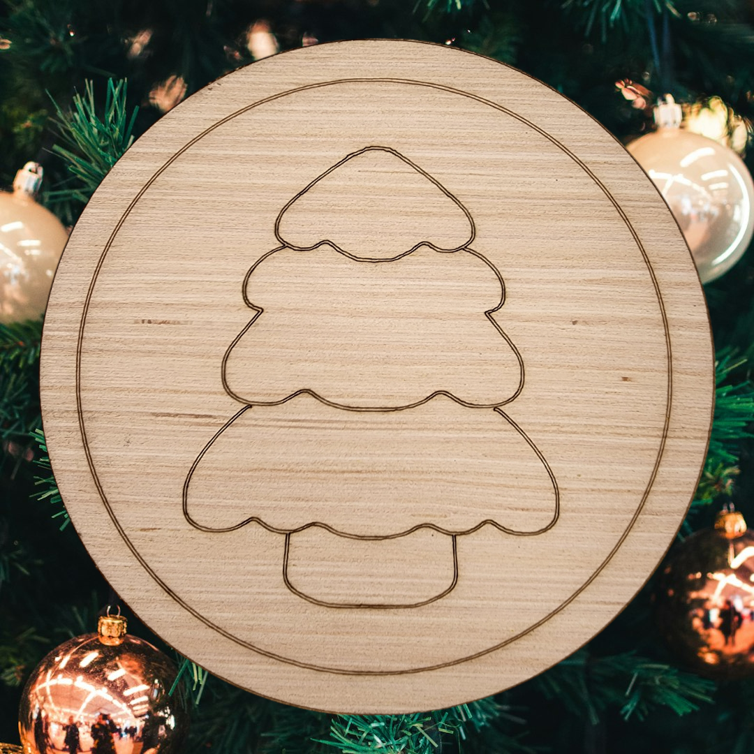 Unfinished round wood blank with an engraved design of a simple Christmas tree.