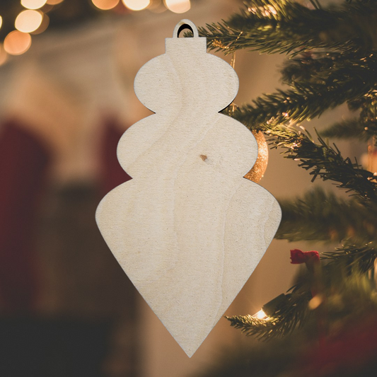 Unfinished wood finial ornament blank hanging in front of a Christmas tree.
